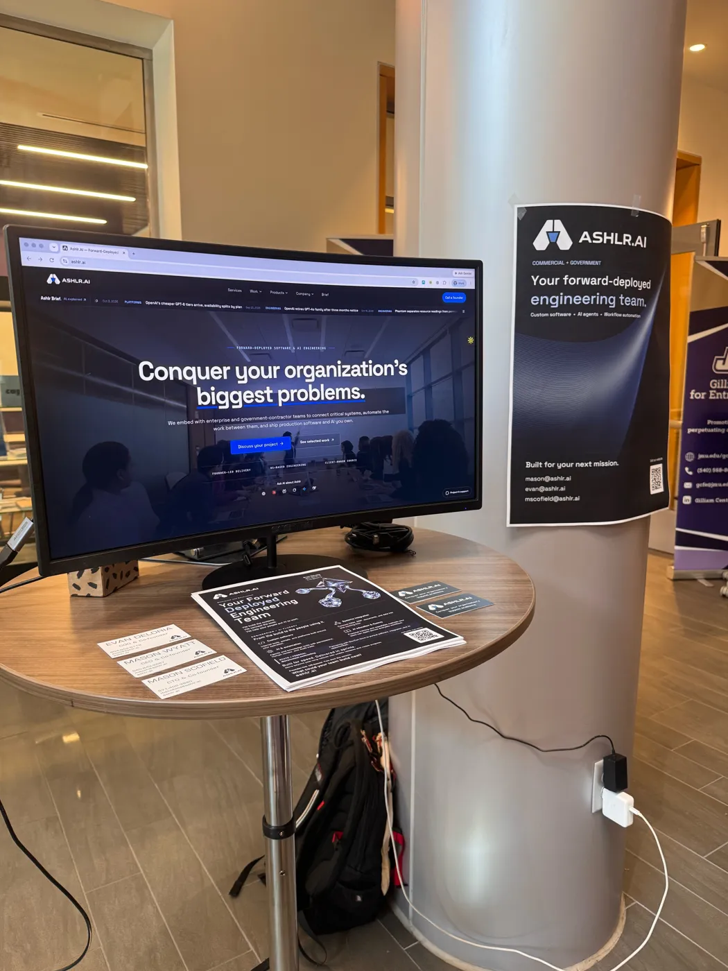The Ashlr booth: a monitor showing the Ashlr website, a poster on the column and printed flyers on a table.